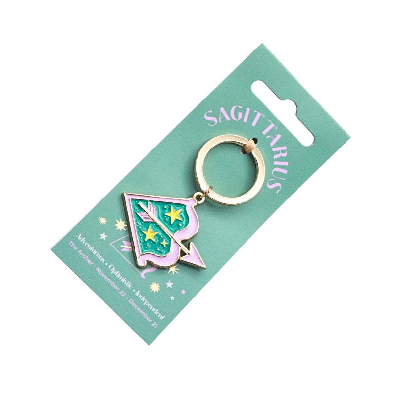 A Sagittarius-themed keychain charm featuring a Christmas tree design with green, pink, and gold enamel, attached to a mint green cardboard display card.