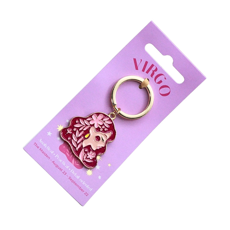 A Virgo-themed enamel keychain charm on a lavender display card. The charm features a pink and red zodiac-themed design with a gold-tone split ring.