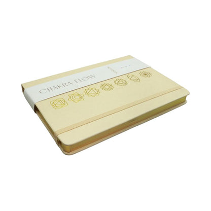 linen cover diary with the chakra symbols printed in gold on the cover. Gold edged pages and a tag with the words "Chakra Flow" and "Notebook" covering it.