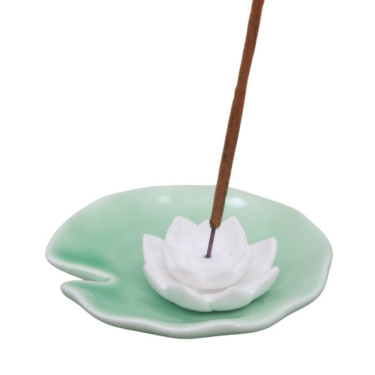 Incense burner shaped like a white lotus on a green base with a single incense stick.