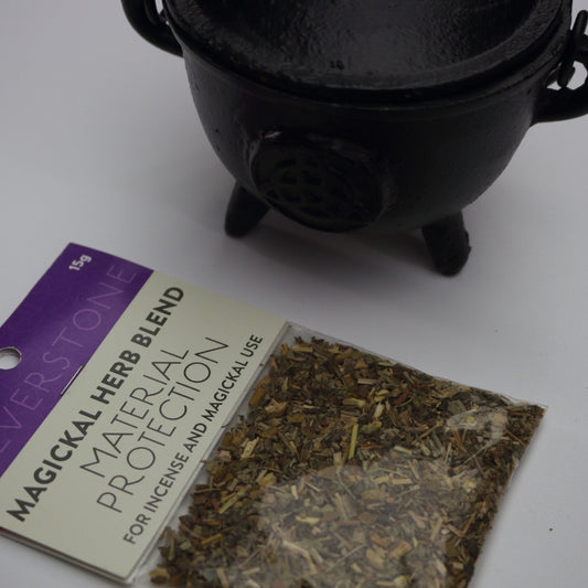 packet of magickal herb blend called material protection sitting in front of a black cauldron