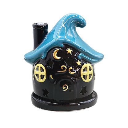 A small decorative ceramic house shaped like a witch's cottage with a bright blue pointed roof, dark blue  body, and gold crescent moon and star details, shown on a plain white background.