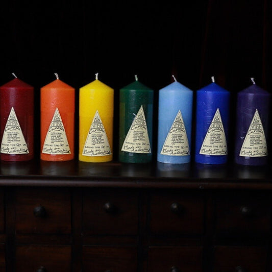 Brightly coloured Nimbin Pillar Candles in a row, on top of a wooden apothecary chest