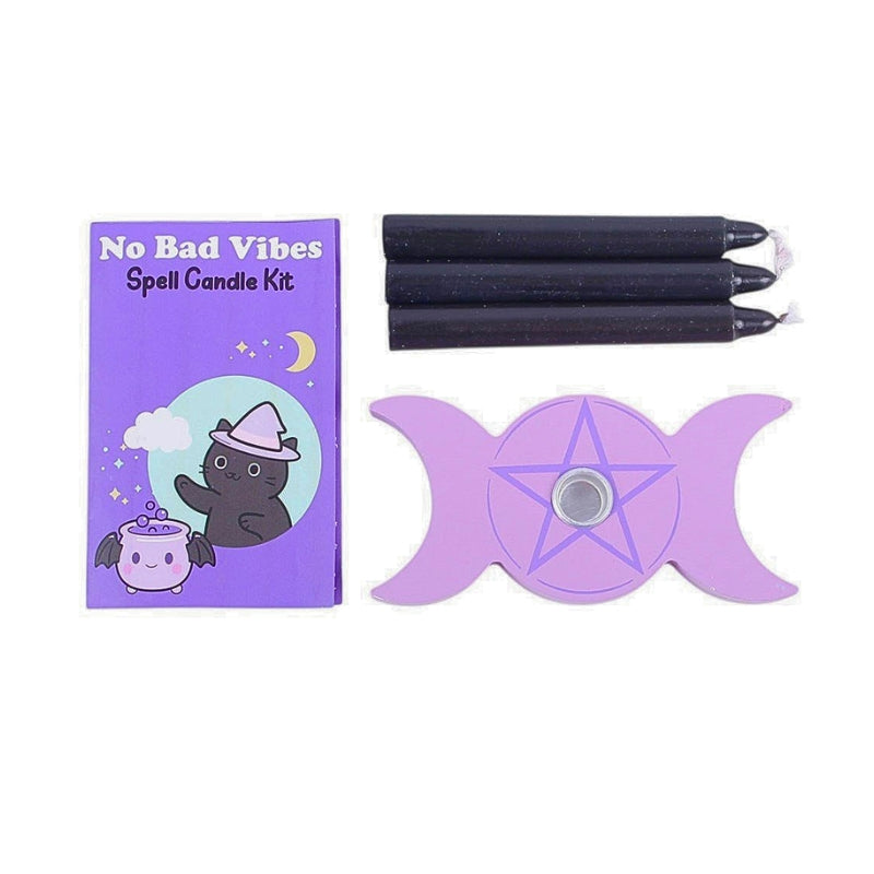 A spell candle kit laid out on a white background, including a purple illustrated box labeled 'No Bad Vibes Spell Candle Kit,' three black candles, and a purple triple moon wand with a pentagram design.