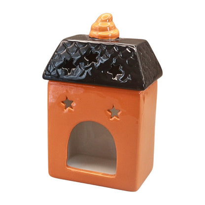 A small ceramic decorative house-shaped vessel with an orange body, a black roof, star-shaped cutouts on the front, and a small orange topper on top, shown on a plain white background.