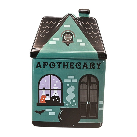 A haunted house shaped ceramic kitchen or bathroom container with 'APOTHECARY' written on the front, featuring illustrated windows, a cauldron, bats, and a black roof on a white background.