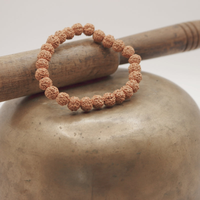 Original Rudraksha Beaded Stretchable Bracelet sitting on an upturned brass singing bowl with wooden striker