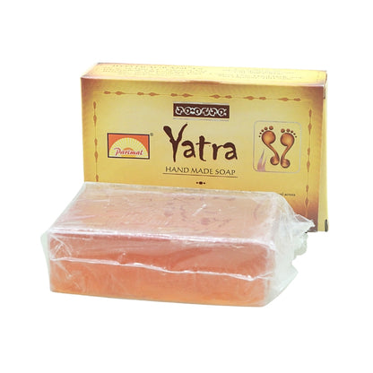 Peach-coloured Parimal Yatra handmade soap bar in clear wrapping, displayed in front of its gold box.