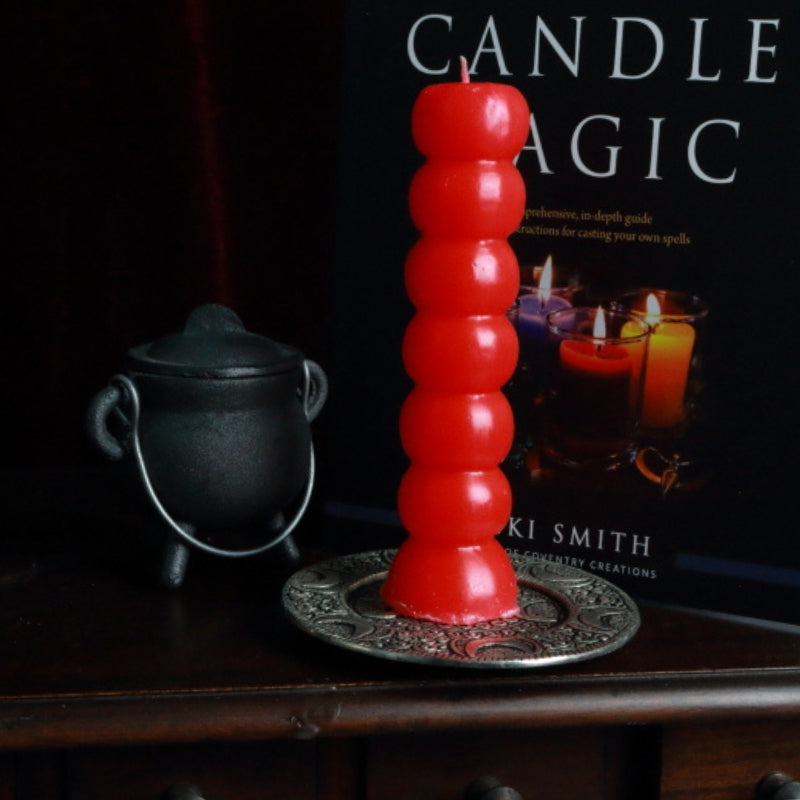 red 7 knob candle on an apothecary cabinet in front of a candle book and cauldron