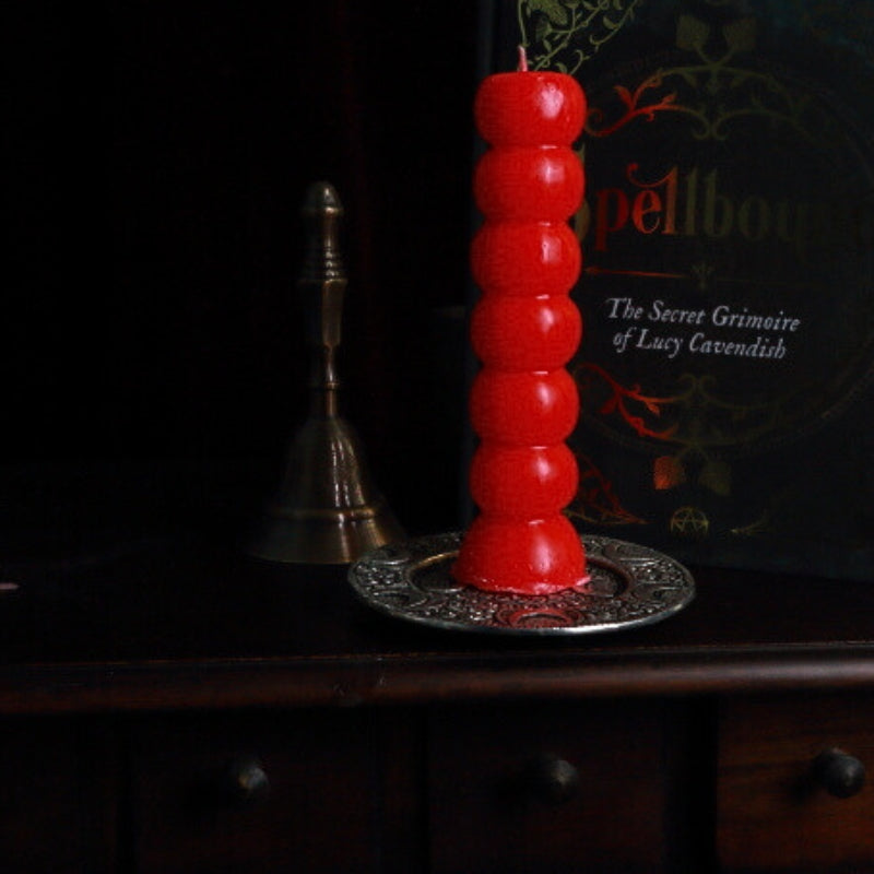 red 7 knob candle on an apothecary cabinet in front of a grimoire and altar bell