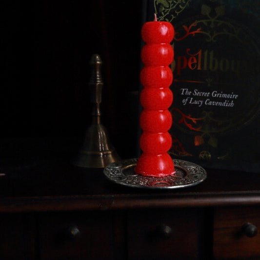 red 7 knob candle on an apothecary cabinet in front of a grimoire and altar bell