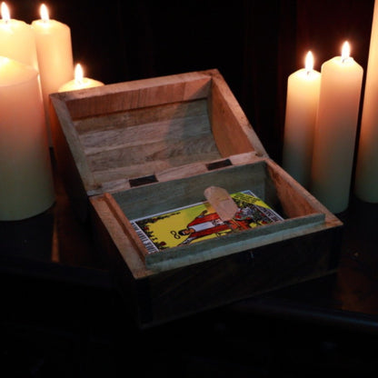lit beeswax pillar candles in the background of an open wooden tarot chest with tarot cards and crystals within