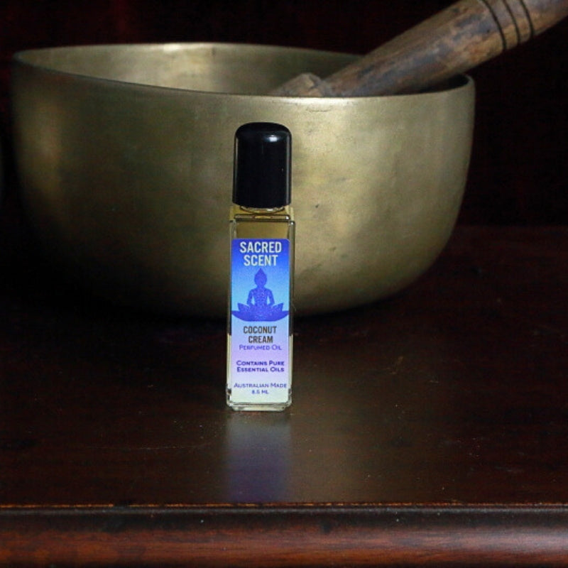 Bottle of Sacred Scents Perfume Oil Coconut Cream sitting on a wooden apothecary cabinet in front of a brass singing bowl