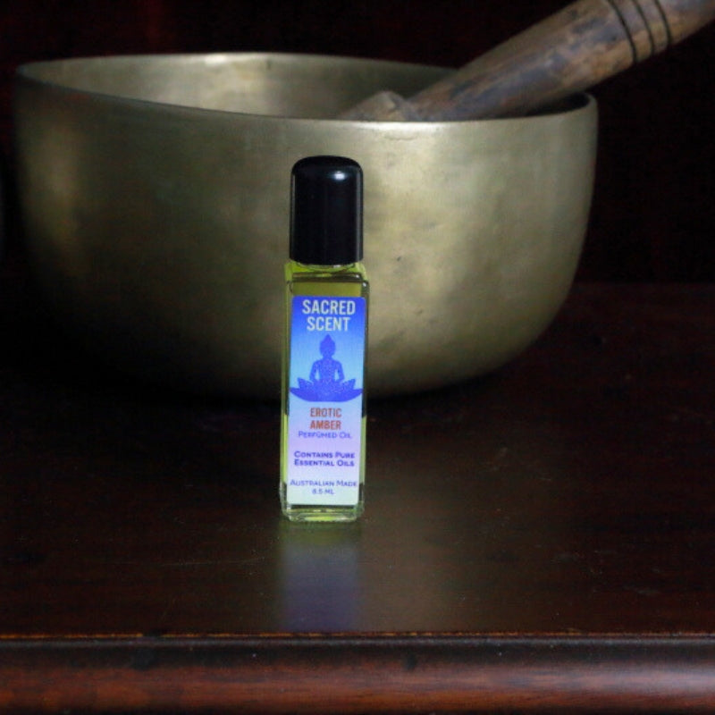 Bottle of Sacred Scents Perfume Oil sitting on a wooden apothecary cabinet in front of a brass singing bowl