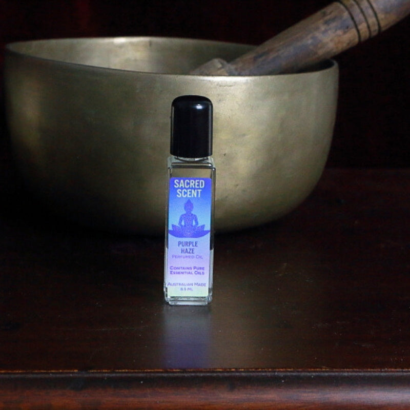 Bottle of Sacred Scents Perfume Oil sitting on a wooden apothecary cabinet in front of a brass singing bowl