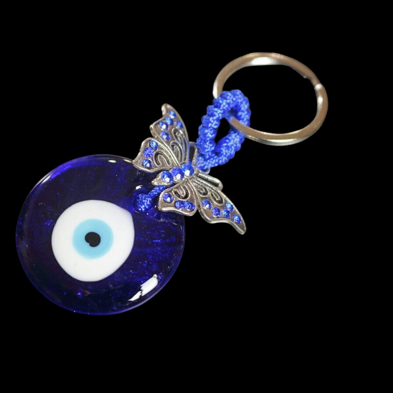 silver key ring attached to a blue cord, a Silver butterfly with blue diamantes, attached to a blue bead with a white and black centre, on a black background