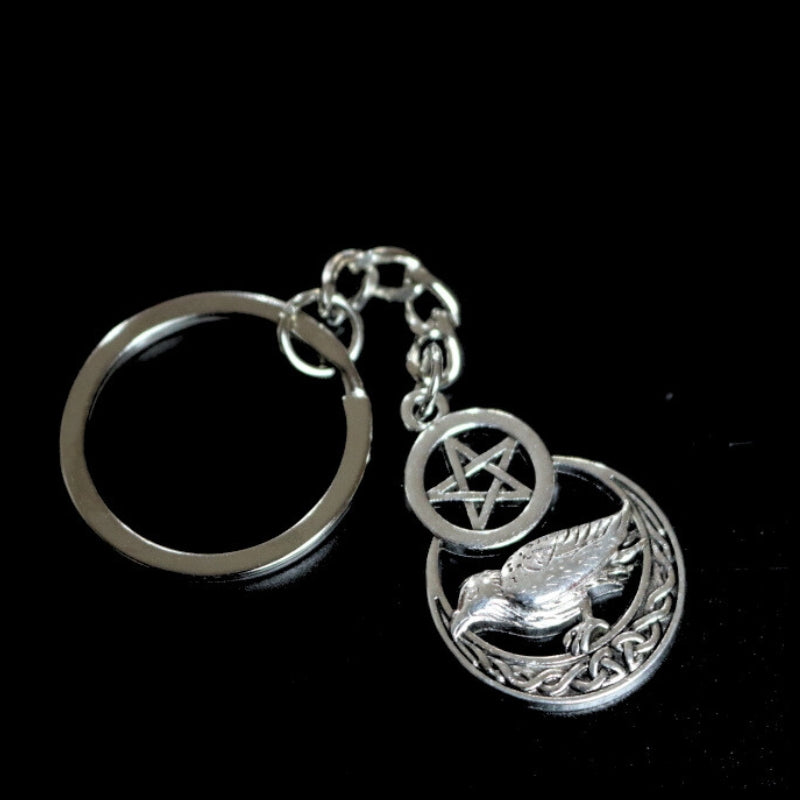 silver coloured key ring with a raven sitting on a crescent moon below a pentacle (5 pointed star within a circle) joined to a silver ring by a silver chain