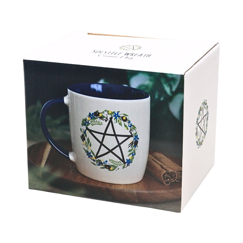 packaging for a cup with cream coloured mug with blue handle and a pentagram design in a floral wreath 