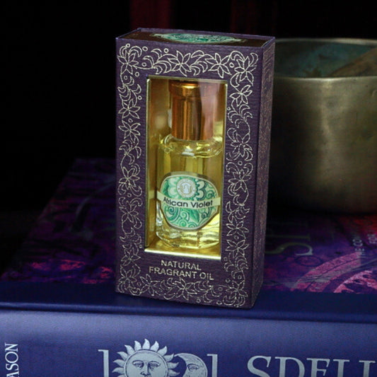 African Violet Song of India Perfume Oil sitting on a book of spells in front of a singing bowl