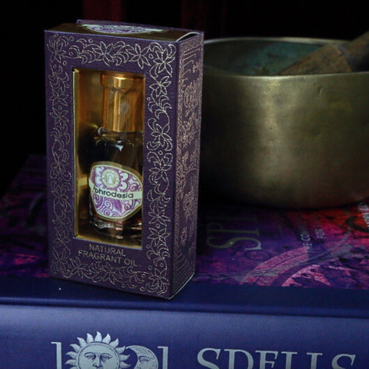 Aphrodesia Song of India Perfume Oil sitting on a book of spells in front of a singing bowl