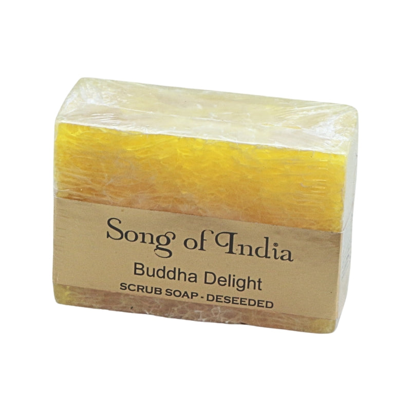 A rectangular bar of yellow deeseed scrub soap wrapped in clear plastic with a brown paper label that reads 'Song of India Buddha Delight SCRUB SOAP - DESEED'.