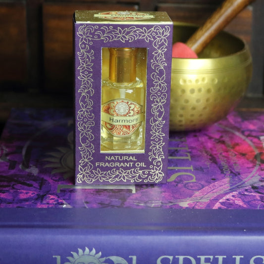 purple and gold box containing a miniature perfume bottle, sitting on a purple and pink book of spells in front of a brass singing bowl with wooden striker. in the background there is an apothecary cabinet