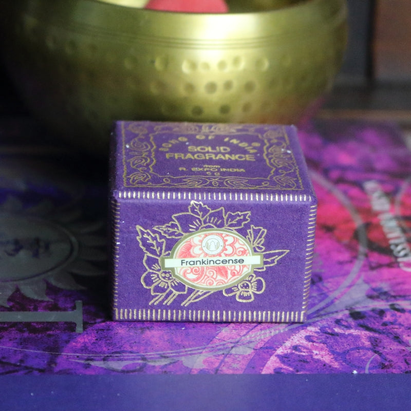 purple and gold box , sitting on a purple and pink book of spells in front of a brass singing bowl with wooden striker.