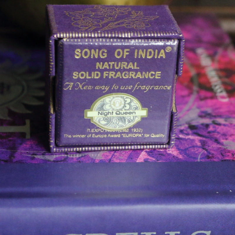 purple and gold box, sitting on a purple and pink book of spells in front of a brass singing bowl with wooden striker.