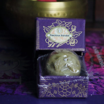 purple and gold box containing a hand carved soapstone jar, sitting on a purple and pink book of spells in front of a brass singing bowl with wooden striker.