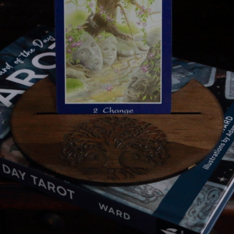 Tree Of Life Tarot Card Holder holding a tarot card. sitting on a "card of the day tarot " book