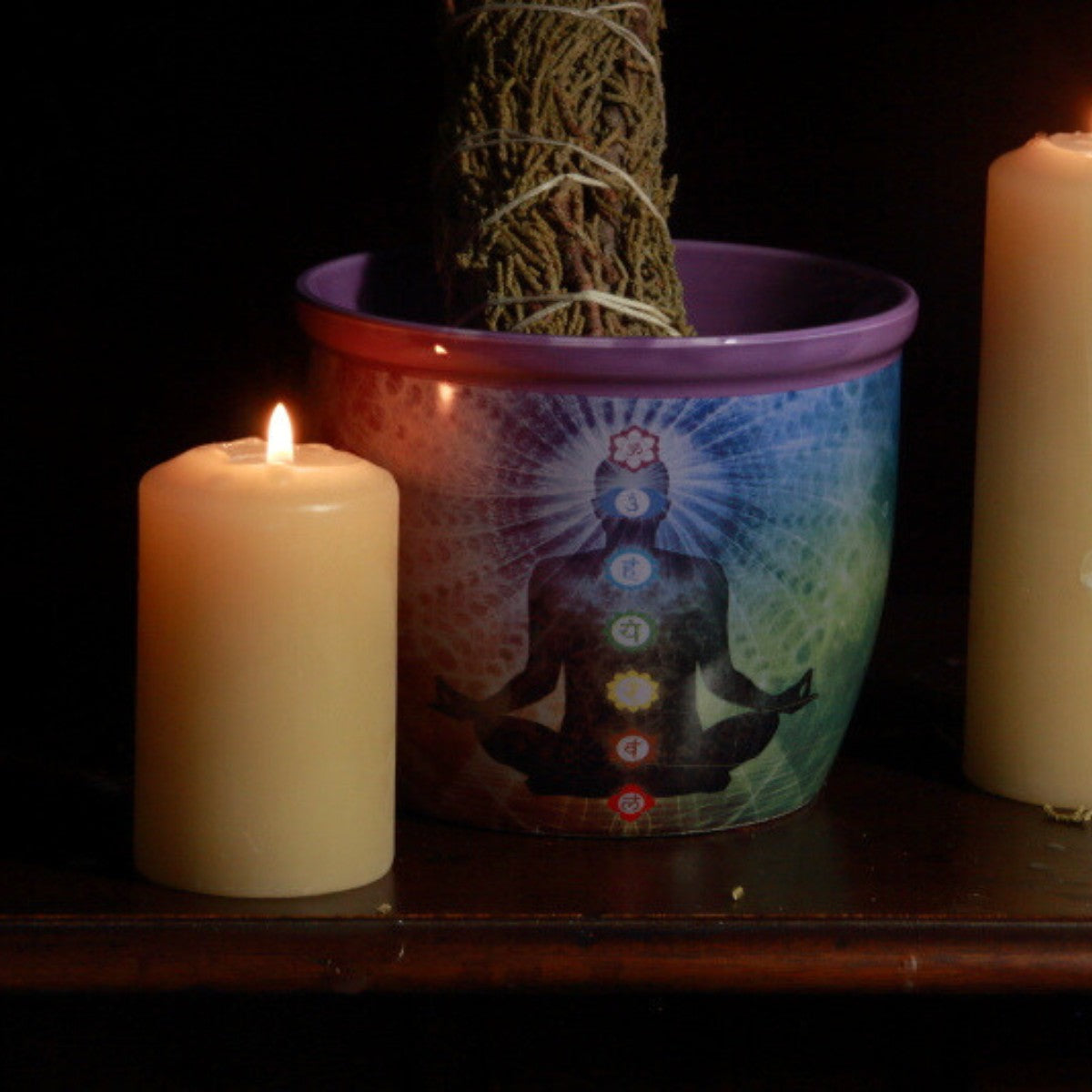 chakra smudge bowl next to beeswax candles with a juniper smudge stick 