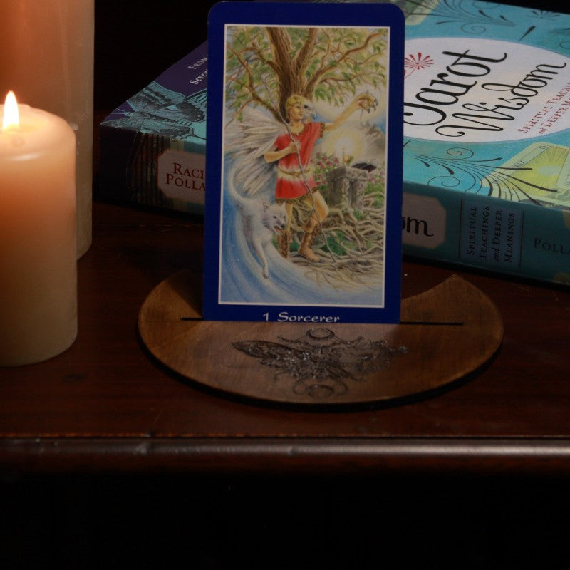 handmade tarot card holder with death moth design, holding an oracle card in front of a tarot book and candles