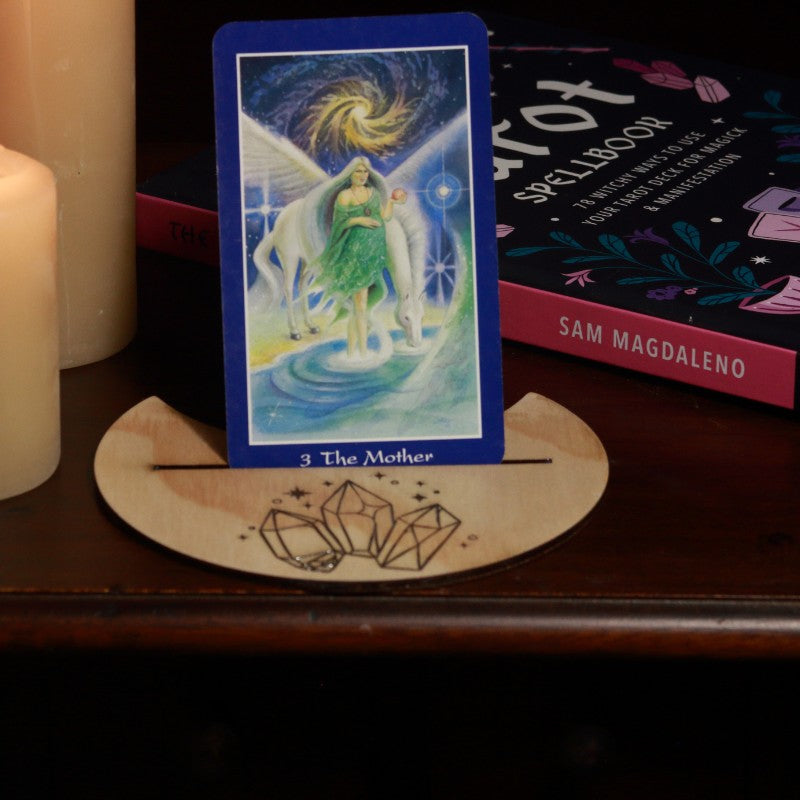 handmade tarot card holder with crystal design holding an oracle card with a tarot book and candles in the background