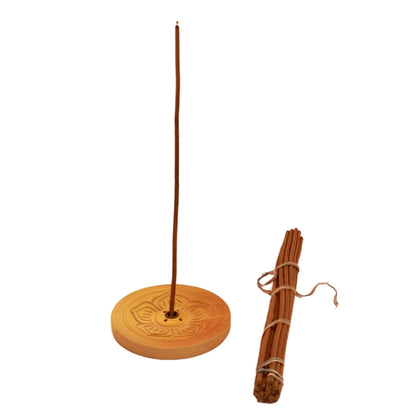 Round wooden carved incense holder- light wood  with a tibetan incense stick in the centre, next to a bundle of tibetan incense sticks