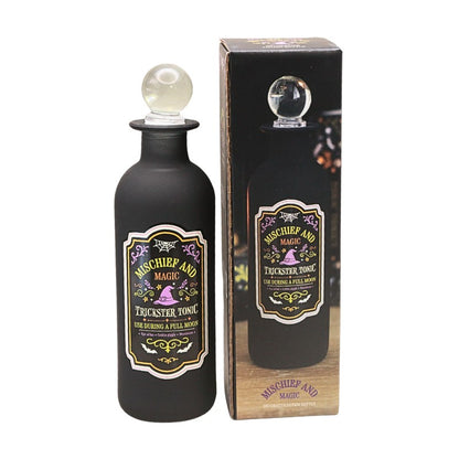 decorative black bottle with round glass stopper and a green and purple spooky design label with witches hat design next to display box
