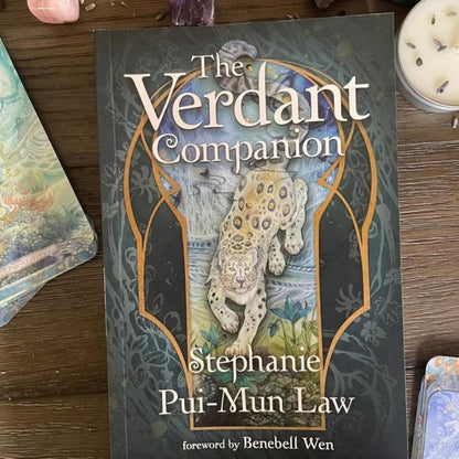 Book titled 'The Verdant Companion' by Stephanie Pui-Mun Law on a wooden surface with tarot cards.