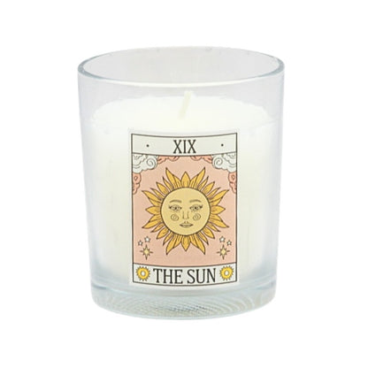 Candle in a glass holder with a tarot card design featuring 'The Sun' card on a white background.