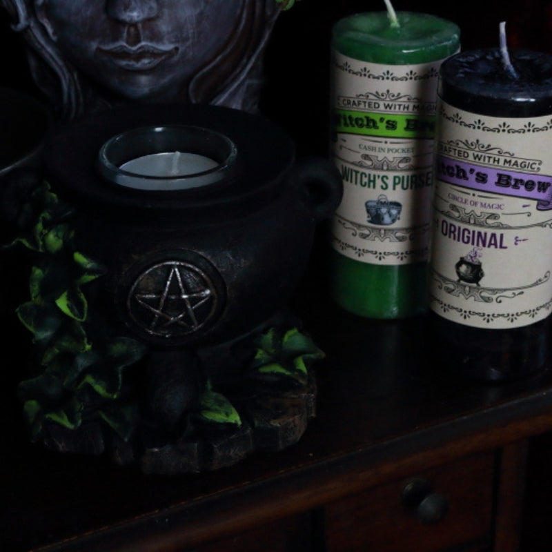 cauldron tealight candle holder in front of a lady planter next to a purple and green coventry creations witch's brew pillar candle