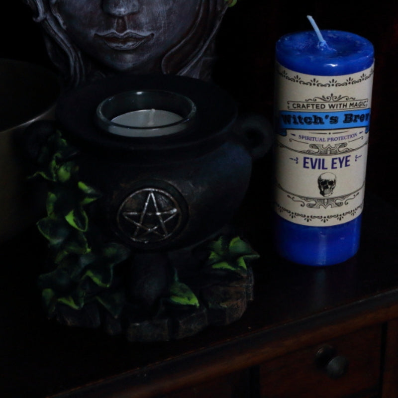 Witch's Brew "evil eye" Pillar Candle next to cauldron candle holder,  lady head planter and brass singing bowl