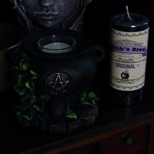 Witch's Brew original Pillar Candle next to cauldron candle holder,  lady head planter and brass singing bowl
