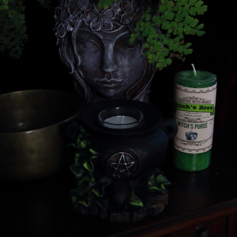 Witch's Brew Witch's Purse Pillar Candle next to cauldron candle holder,  lady head planter and brass singing bowl