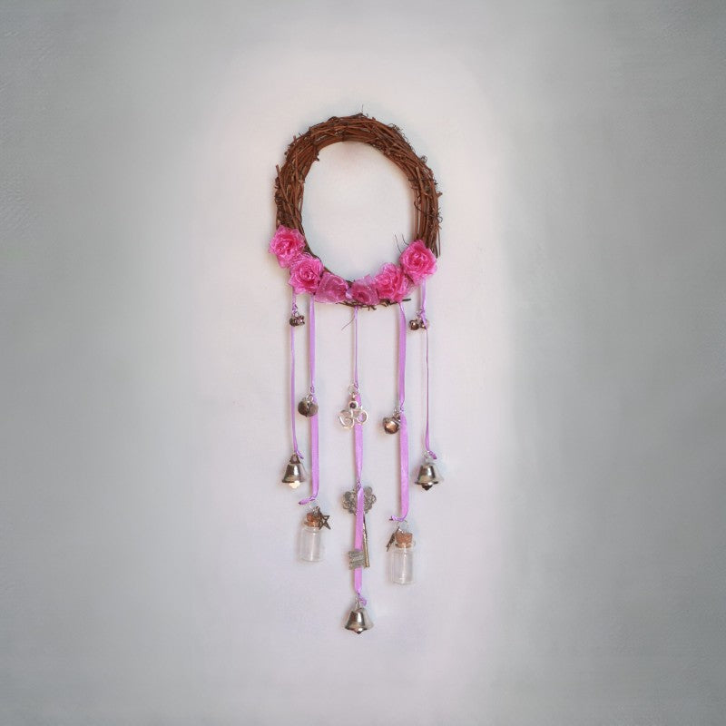 Decorative wall hanging with pink flowers, small bells, and glass bottles on a gray background