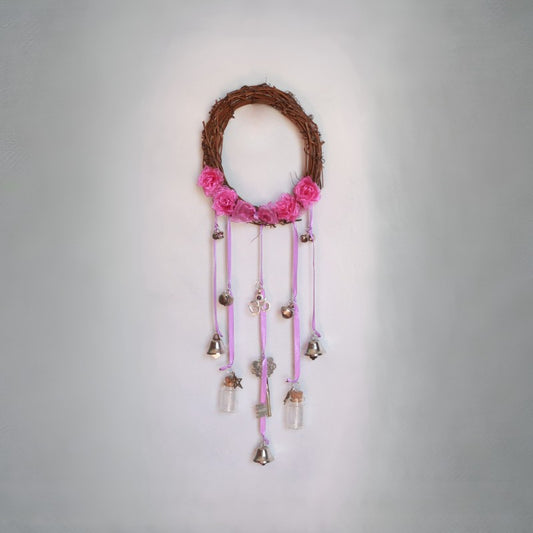 Decorative wall hanging with pink flowers, small bells, and glass bottles on a gray background