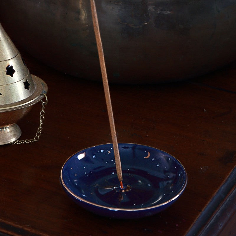 Incense stick burning on a blue dish with a silver incense holder in the background.