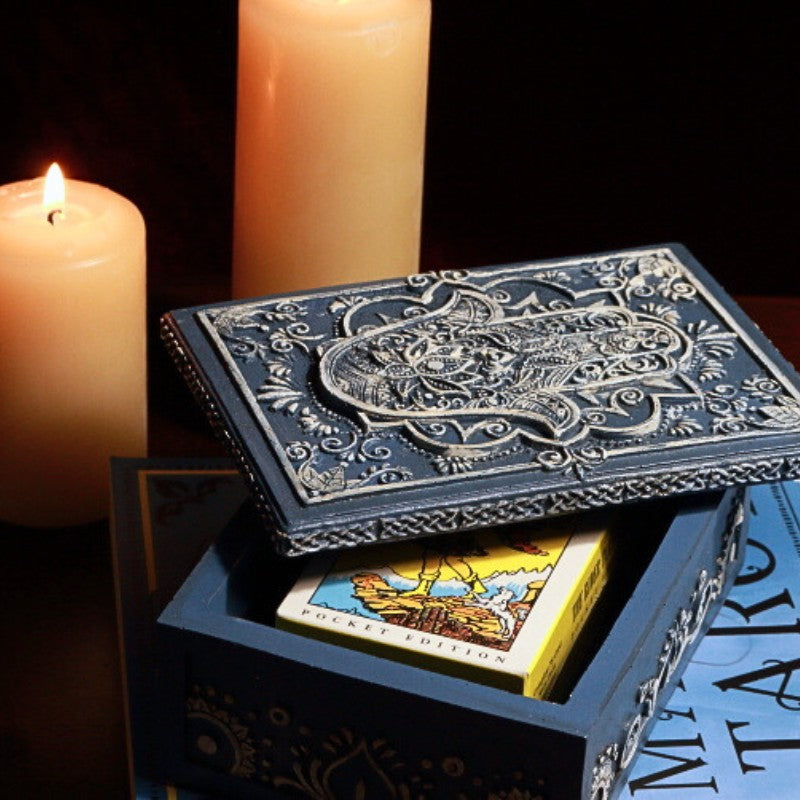 Blue Hamsa Tarot Card Storage Box with a pack of pocket sized rider waite tarot cards in front of beeswax candles on a tarot book