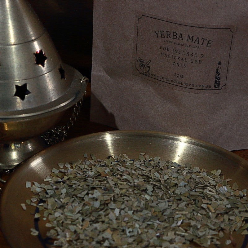 Yerba Mate leaves on a metal tray with a metal cone and packaging in the background.