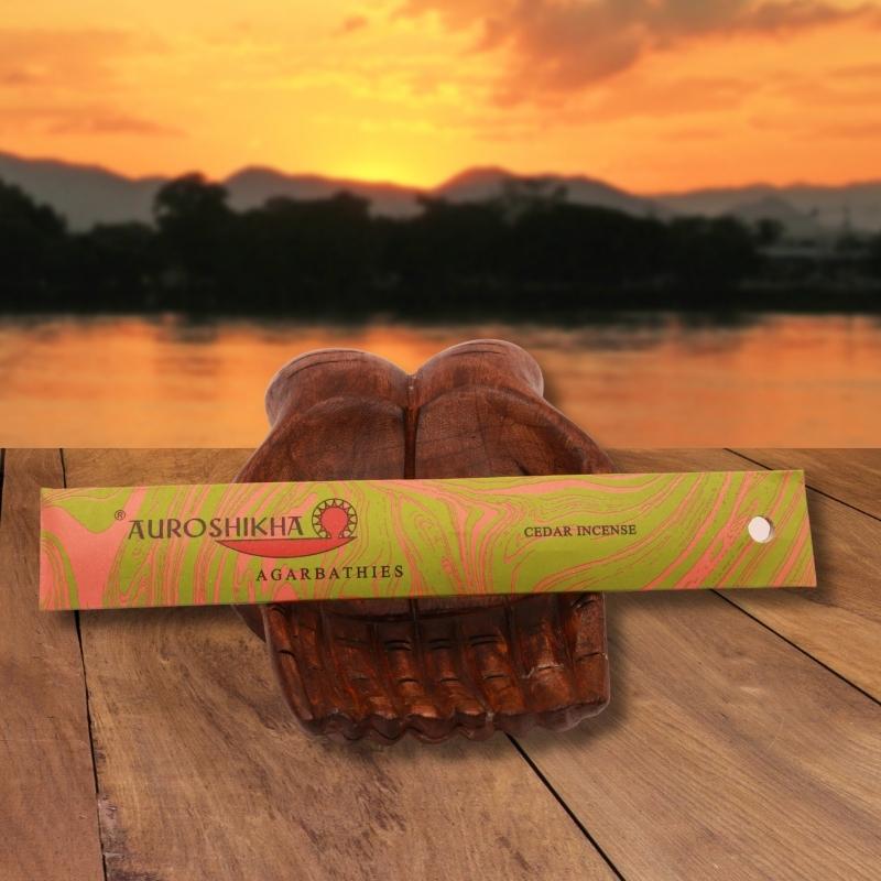 pk of auroshikha incense sitting on a carved wooden hand on a jetty, in front of a golden sunset