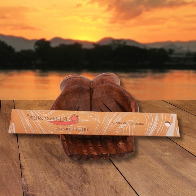 pk of auroshikha incense sitting on a carved wooden hand on a jetty, in front of a golden sunset