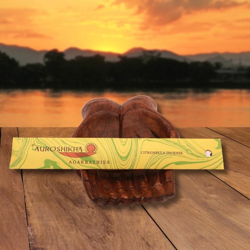 pk of auroshikha incense sitting on a carved wooden hand on a jetty, in front of a golden sunset