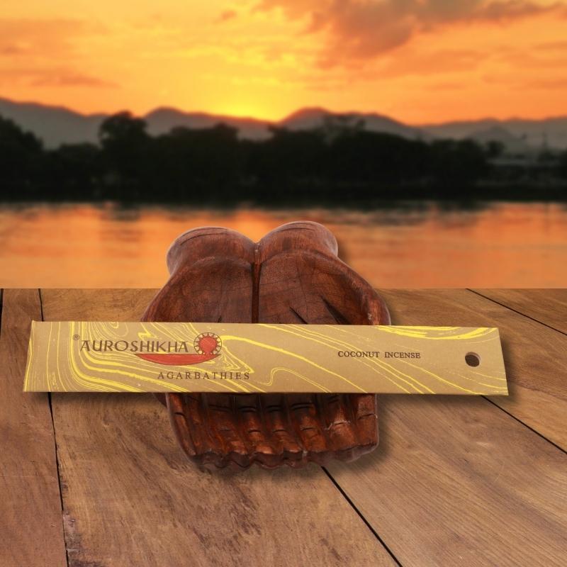 pk of auroshikha incense sitting on a carved wooden hand on a jetty, in front of a golden sunset